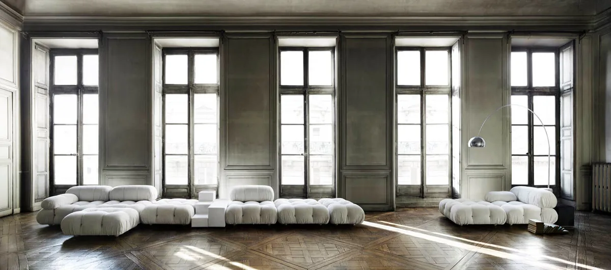 Camaleonda in cream fabric in a high-ceiling paneled room, modular seating along a run of windows