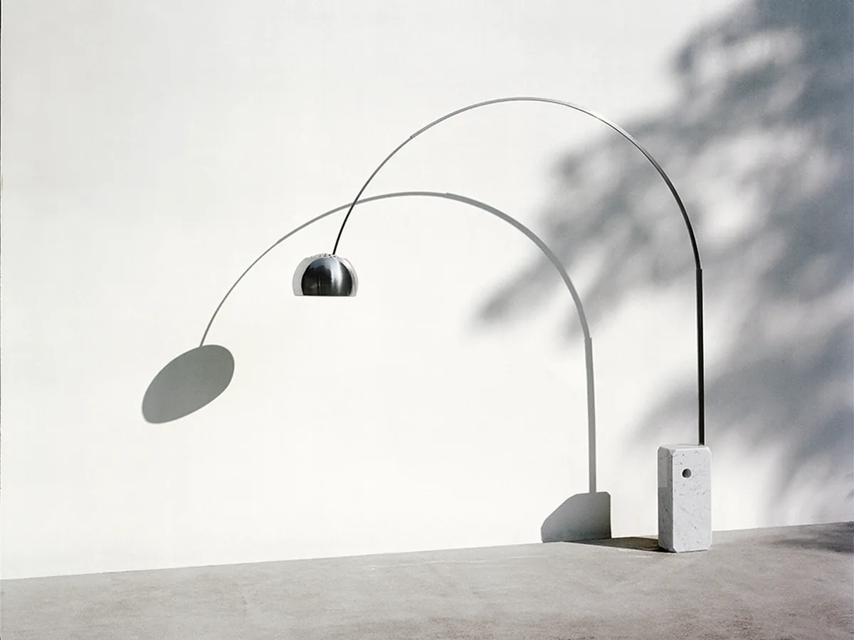 Arco Led in a bright interior, marble base and stainless arc casting a graphic shadow on a white wall
